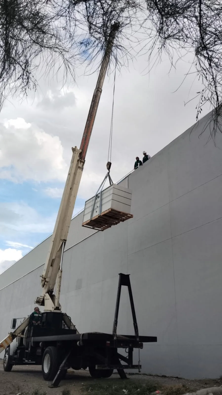 Subida de material a la azotea de una nave industrial, con grúa sobre camión
